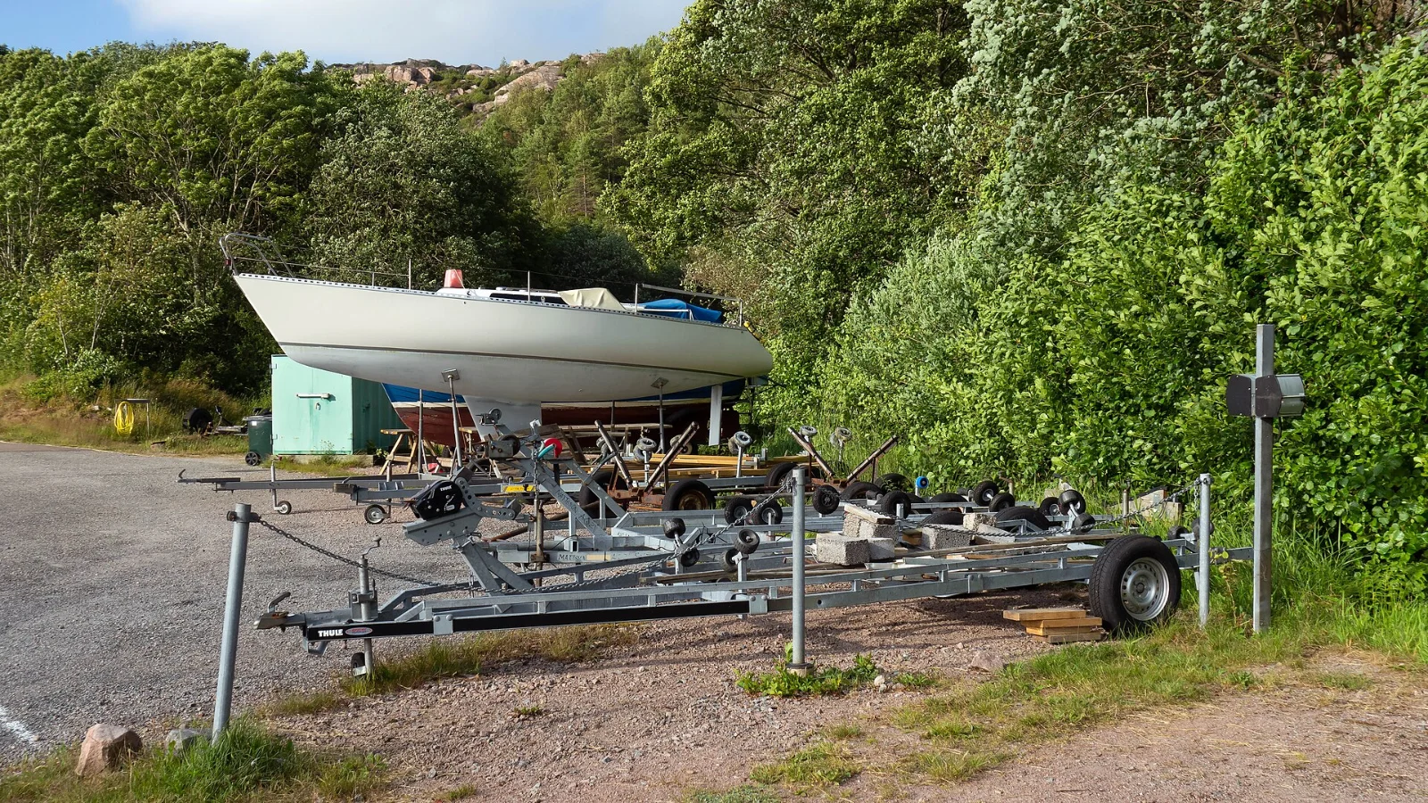 Båthengere parkert på land ved en marina med en seilbåt i bakgrunnen