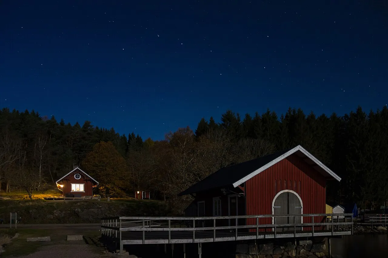 Båtklubb med rødt naust og flytebrygge i måneskinn under stjernehimmel